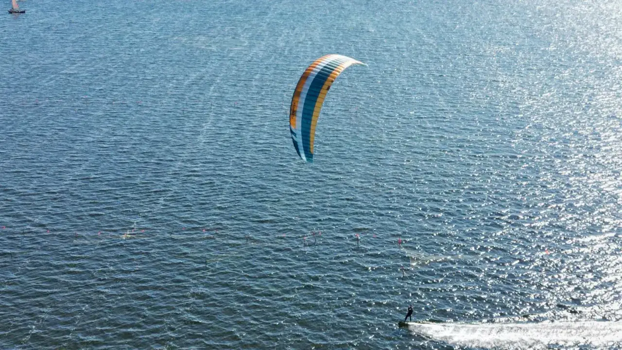 Kitesurfer ślizga się po falach, ciesząc się ekscytującymi sportami wodnymi. Kolorowy latawiec unosi się nad wodą.