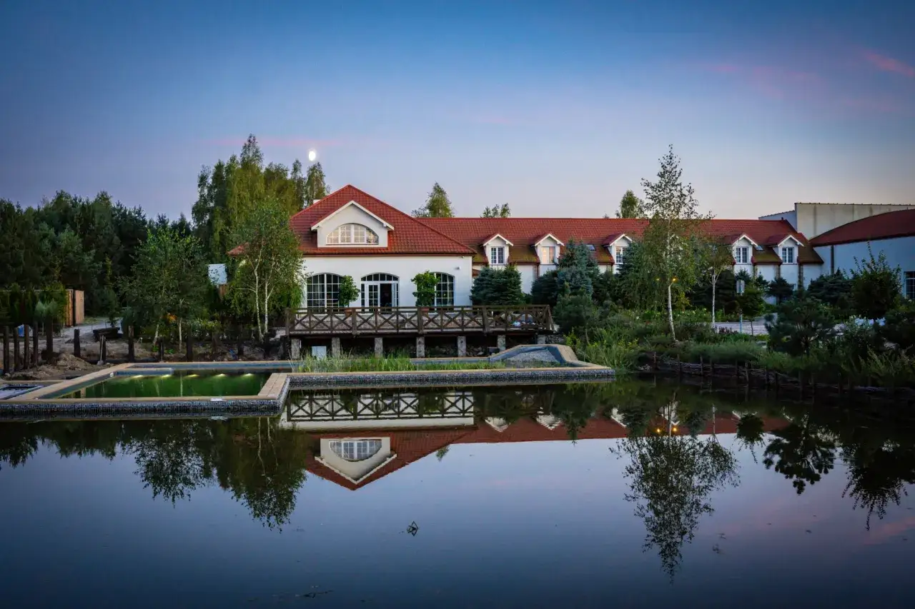 Malowniczy hotel spa lubelskie z basenem i odbiciem w stawie o zmierzchu.