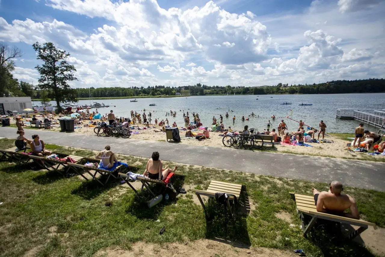 Plaża nad jeziorem w Kiekżu tętni życiem. Ludzie opalają się, kąpią i odpoczywają na leżakach.