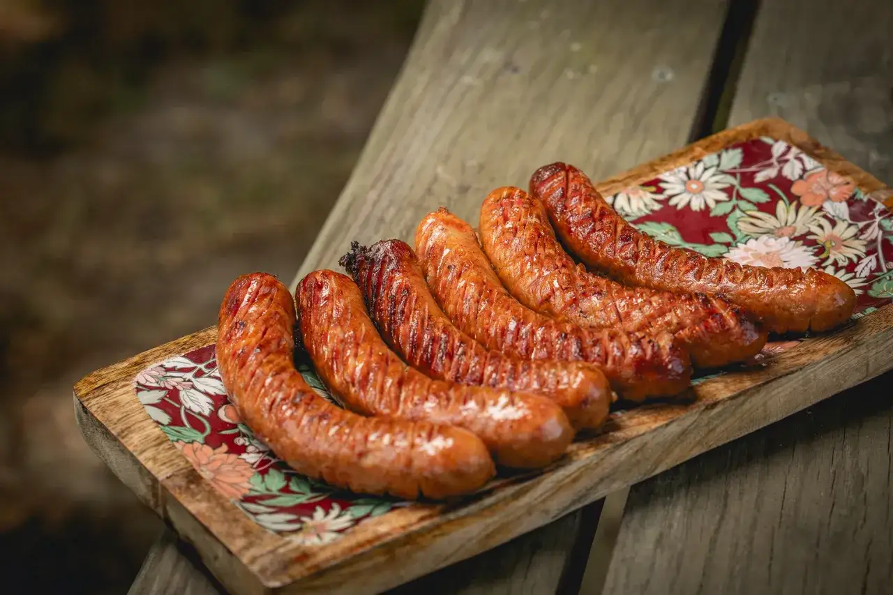 Apetyczna kiełbasa na grilla, rumiana i soczysta, ułożona na drewnianej desce z kolorowym wzorem.