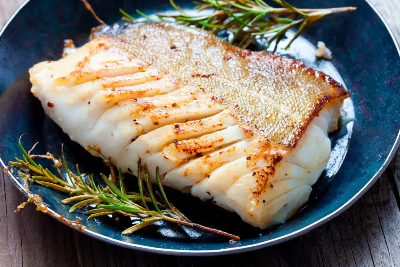 Zdrowa ryba zębacz, soczysty filet z chrupiącą skórką, podany z rozmarynem na ciemnym talerzu.