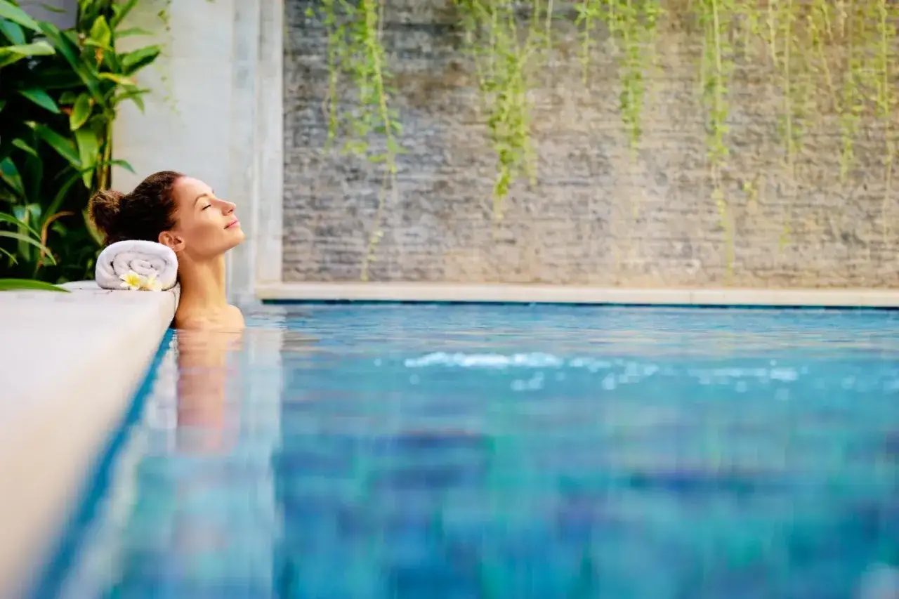 Kobieta relaksuje się w basenie hotelowego spa w Krakowie. Ręcznik z kwiatem podtrzymuje jej głowę.