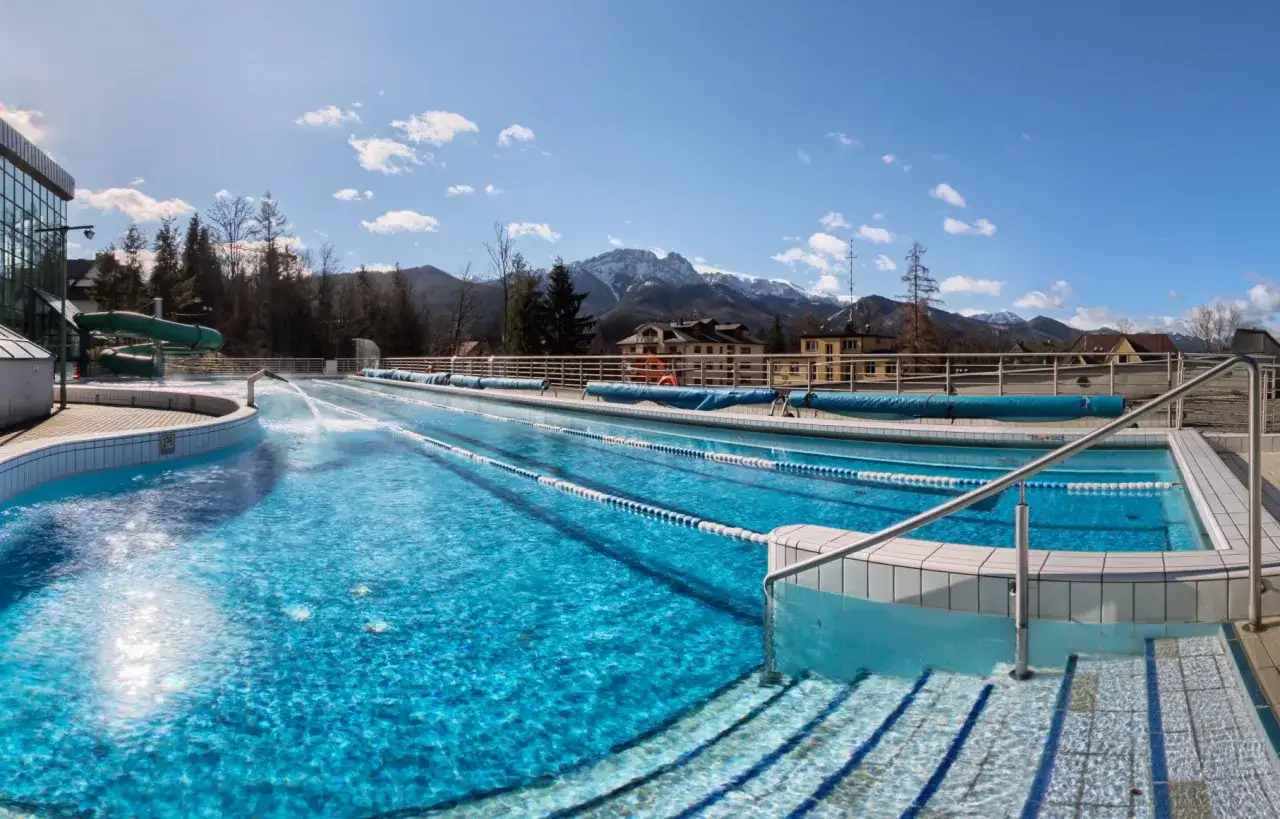 Basen zewnętrzny z widokiem na Tatry, idealny dla hoteli w Zakopanem z basenem. Woda kusi błękitem, a w tle majaczą ośnieżone szczyty.