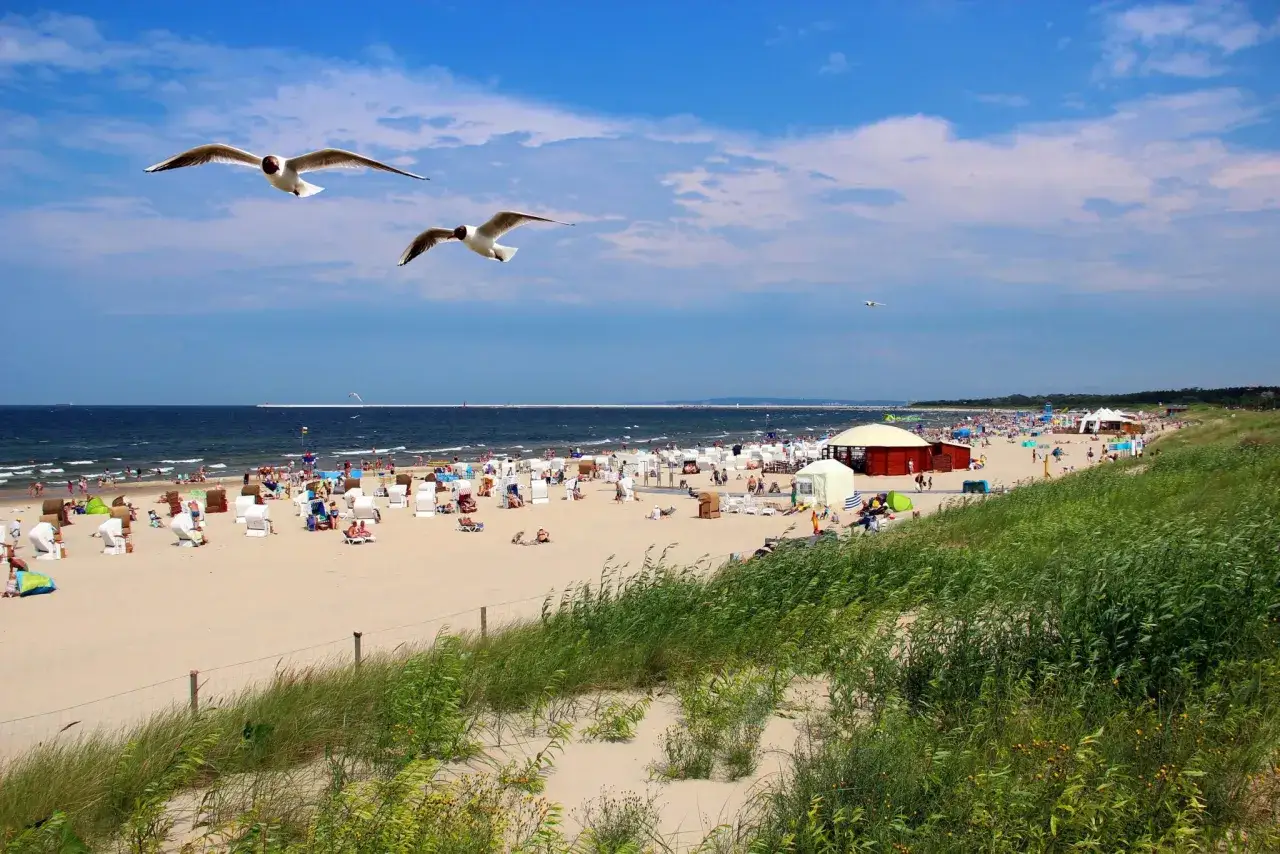 Słoneczna plaża w Świnoujściu z mnóstwem ludzi, mewami na niebie i budkami plażowymi. Idealne świnoujście atrakcje dla dzieci.