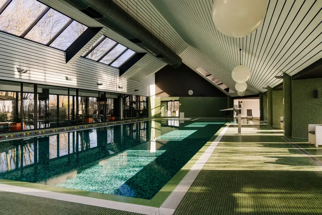 Basen w hotelu spa lubelskie. Duże okna, zielone mozaiki i drewniany sufit tworzą relaksującą atmosferę.