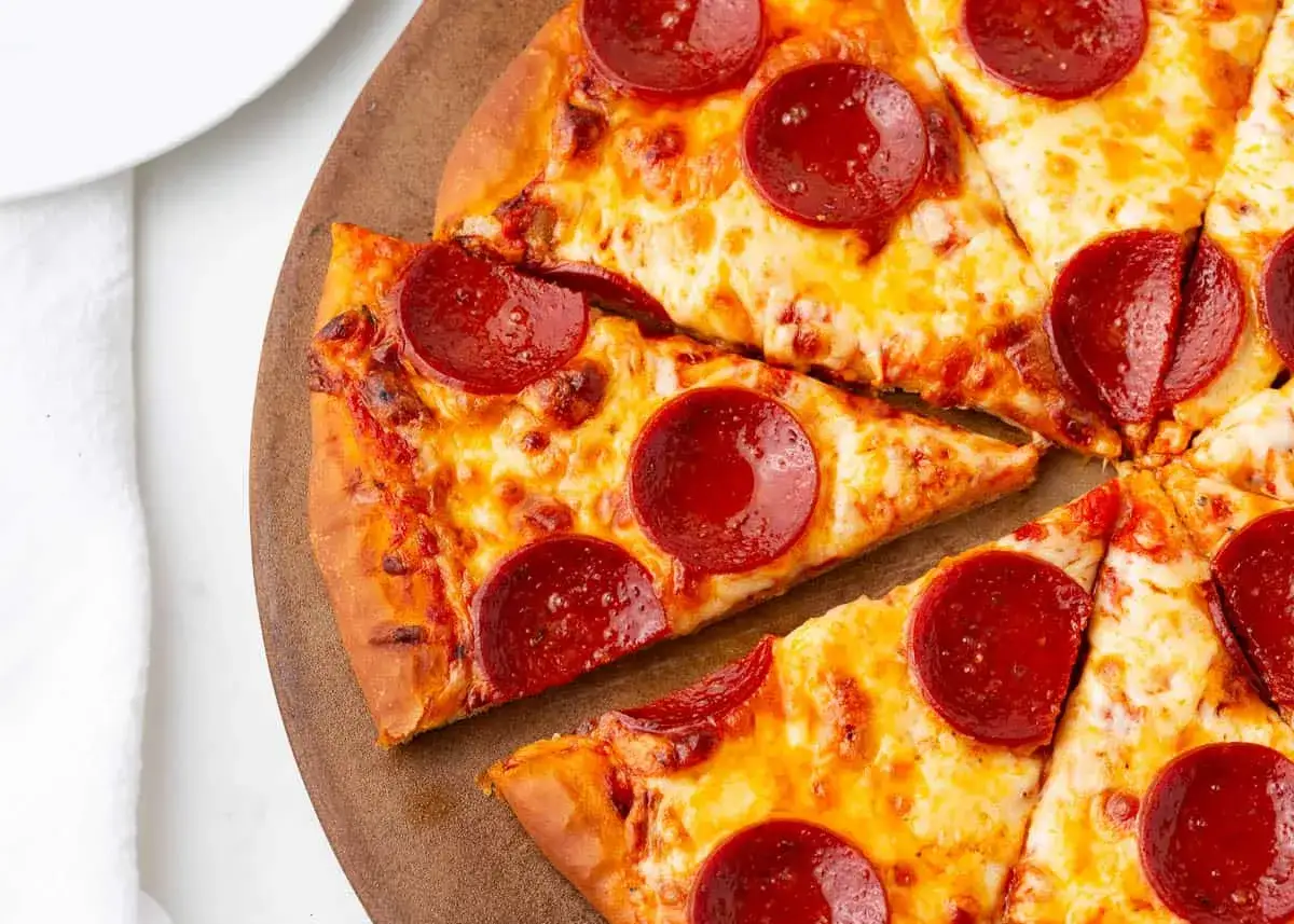 Apetyczna pizza pepperoni na drewnianej desce, z ciągnącym się serem i chrupiącymi brzegami.
