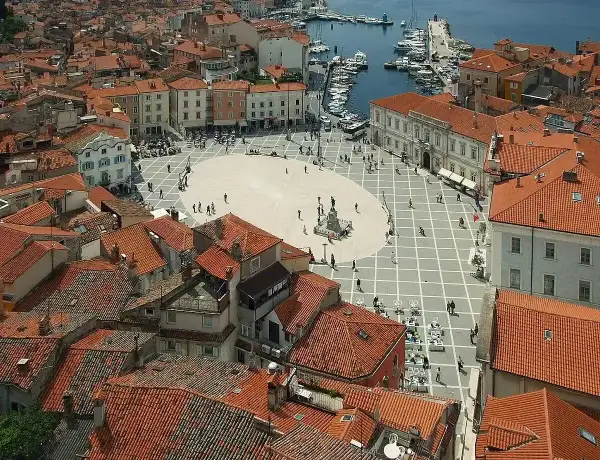 Widok na plac w Piran, Słowenia, z widokiem na morze i port. Czerwone dachy i zabytkowa architektura tworzą malowniczy krajobraz.