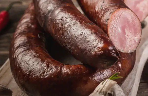 Kiełbasa lisiecka, wędzona, z widocznym przekrojem ukazującym różowe mięso. Obok czosnek i papryczka chili.
