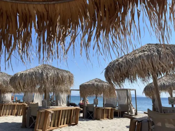 Słomiane parasole i leżaki na plaży Tigaki, z widokiem na spokojne, błękitne morze i bezchmurne niebo.