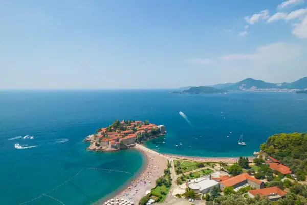 Sveti Stefan, Czarnogóra, z widokiem na turkusowe morze i zatłoczoną plażę.