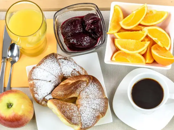 Idealne śniadanie kontynentalne: świeże croissanty, sok pomarańczowy, kawa, owoce i dżem.
