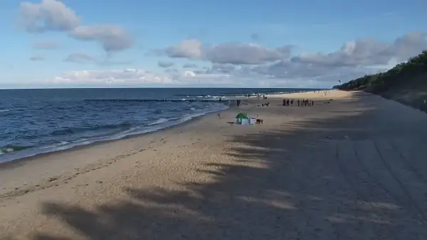 Piękny zachód słońca w Pobierowie. Ludzie spacerują po plaży, morze faluje, a niebo zdobią chmury.