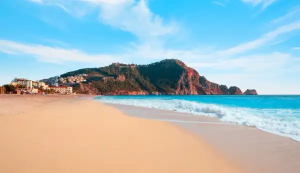 Piękna plaża Kleopatry z turkusową wodą i skalistym cyplem, na którym widać ruiny zamku.