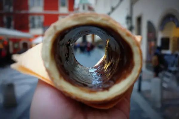 Trdelník z czekoladą, jeden z pysznych czeskich przysmaków, widziany przez jego wnętrze na tle ulicy.