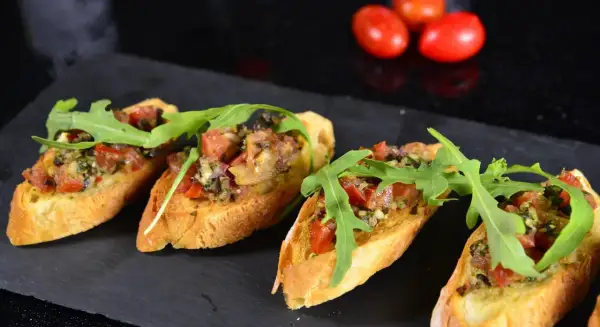 Cztery chrupiące **tapas** z pomidorami, ziołami i rukolą na ciemnej desce.
