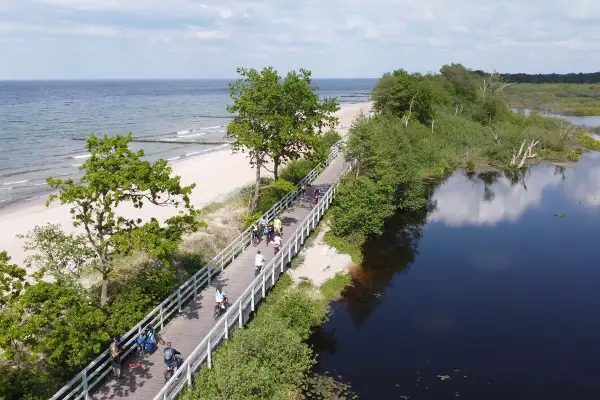 Ludzie na rowerach przemierzają malowniczą trasę Velo Baltica wzdłuż plaży i spokojnej wody.